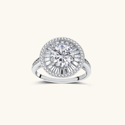 Brilliant round moissanite center stone with baguette and round halo accents in sterling silver setting on light background.