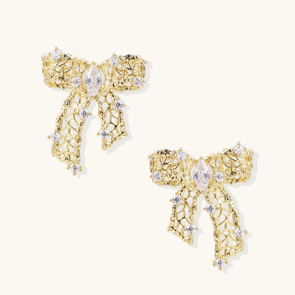 Gold-plated bow earrings with openwork design, marquise center stones, and flowing ribbon tails adorned with zirconia crystals.