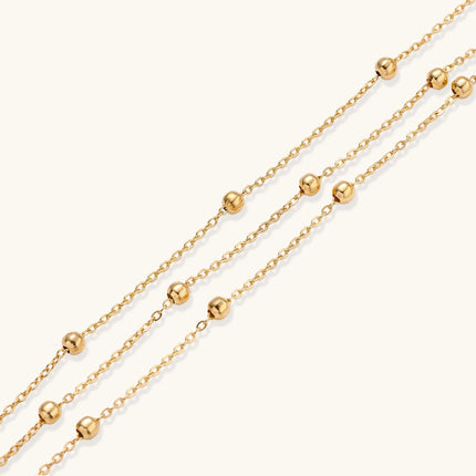 Three-strand gold-plated bracelet with clustered ball beads and adjustable clasp on cream background