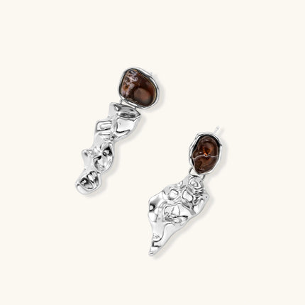 Abstract sculptural silver earrings with brown resin stones featuring organic fluid metalwork design on white background.