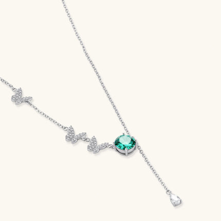 Sterling silver necklace with butterfly charms, green moissanite center stone, and teardrop crystal pendant on white background.