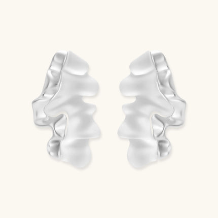 Pair of silver-toned sculptural earrings with flowing abstract forms and stud backs against white background.