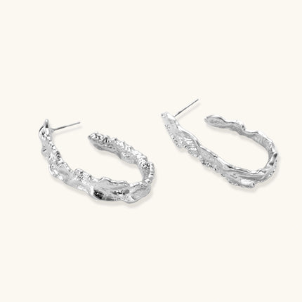 Close-up of textured silver hoop earrings with twisted rope-like pattern and post-back closure on white background.