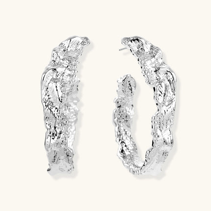 Close-up of textured silver hoop earrings with twisted rope-like pattern and post-back closure on white background.