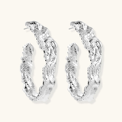 Close-up of textured silver hoop earrings with twisted rope-like pattern and post-back closure on white background.