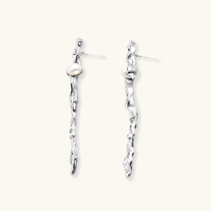 Sculptural silver drop earrings with flowing twisted design and white pearls on neutral background.