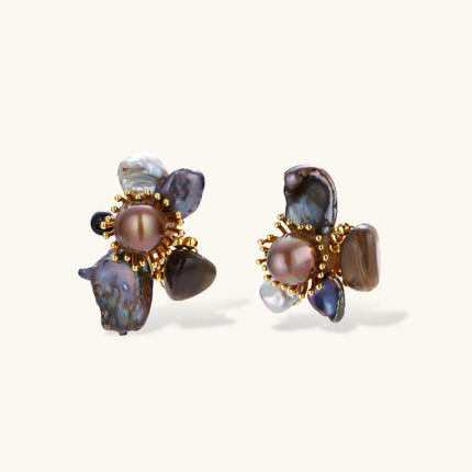 Dark baroque pearl cluster earrings with gold sunburst centers arranged in organic floral design on cream background.