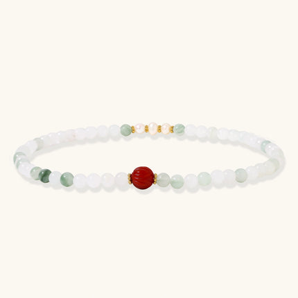 Three layered white beaded bracelets with carved orange agate lotus centerpiece and freshwater pearls on cream background.