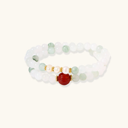 Three layered white beaded bracelets with carved orange agate lotus centerpiece and freshwater pearls on cream background.