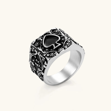 Silver-tone 316L stainless steel signet ring with black enamel spade motif and intricate floral scrollwork relief detail.